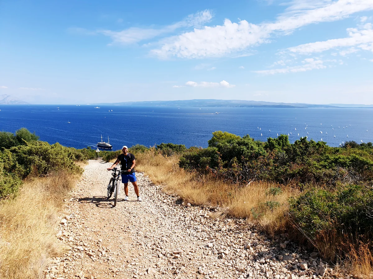 Ante riding along a gravel coastal path on Čiovo with the sea and coast behind