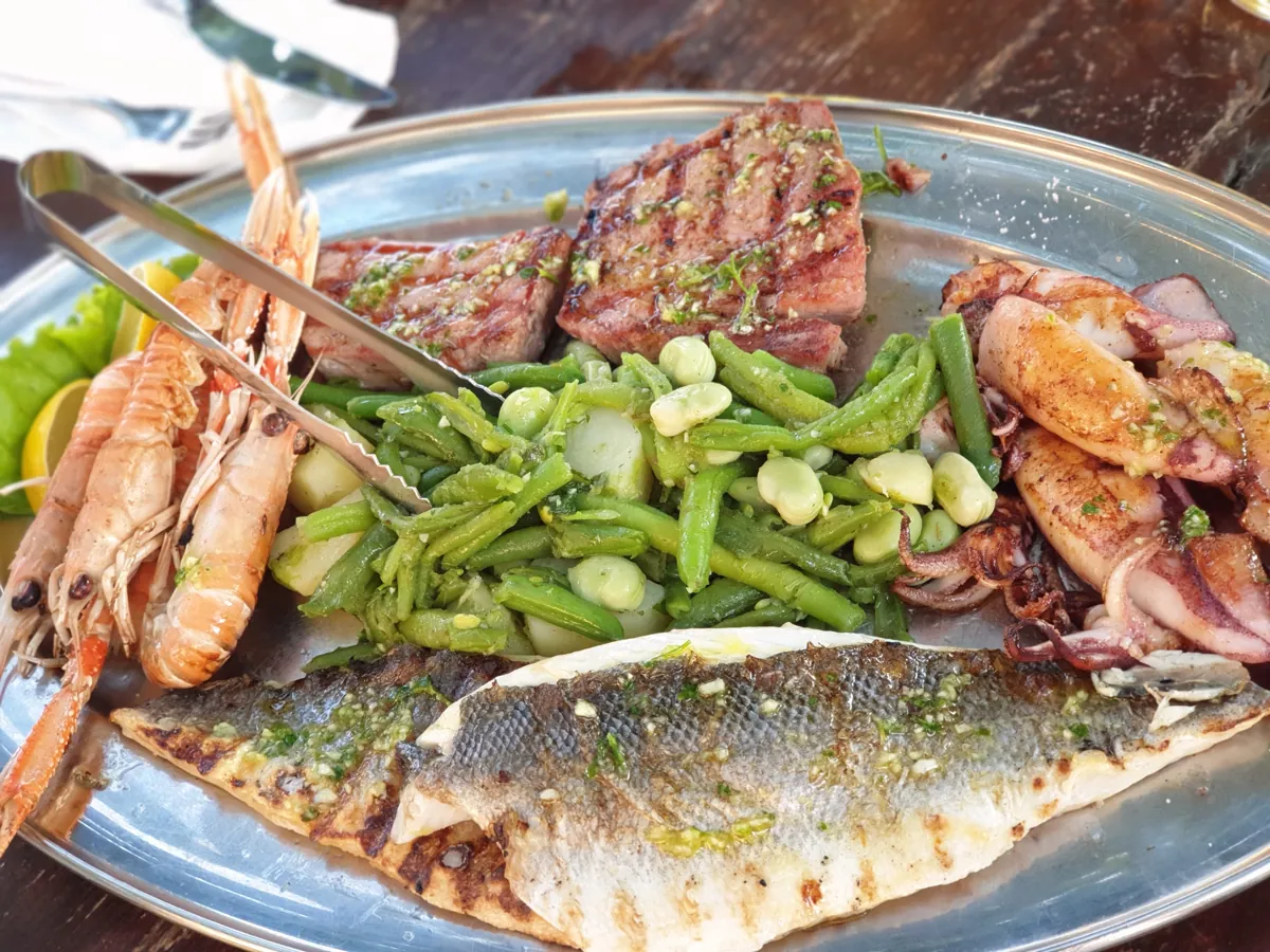 Ein ganzer gegrillter Fisch mit gegrillter Zucchini und Frühlingszwiebeln auf einem Teller