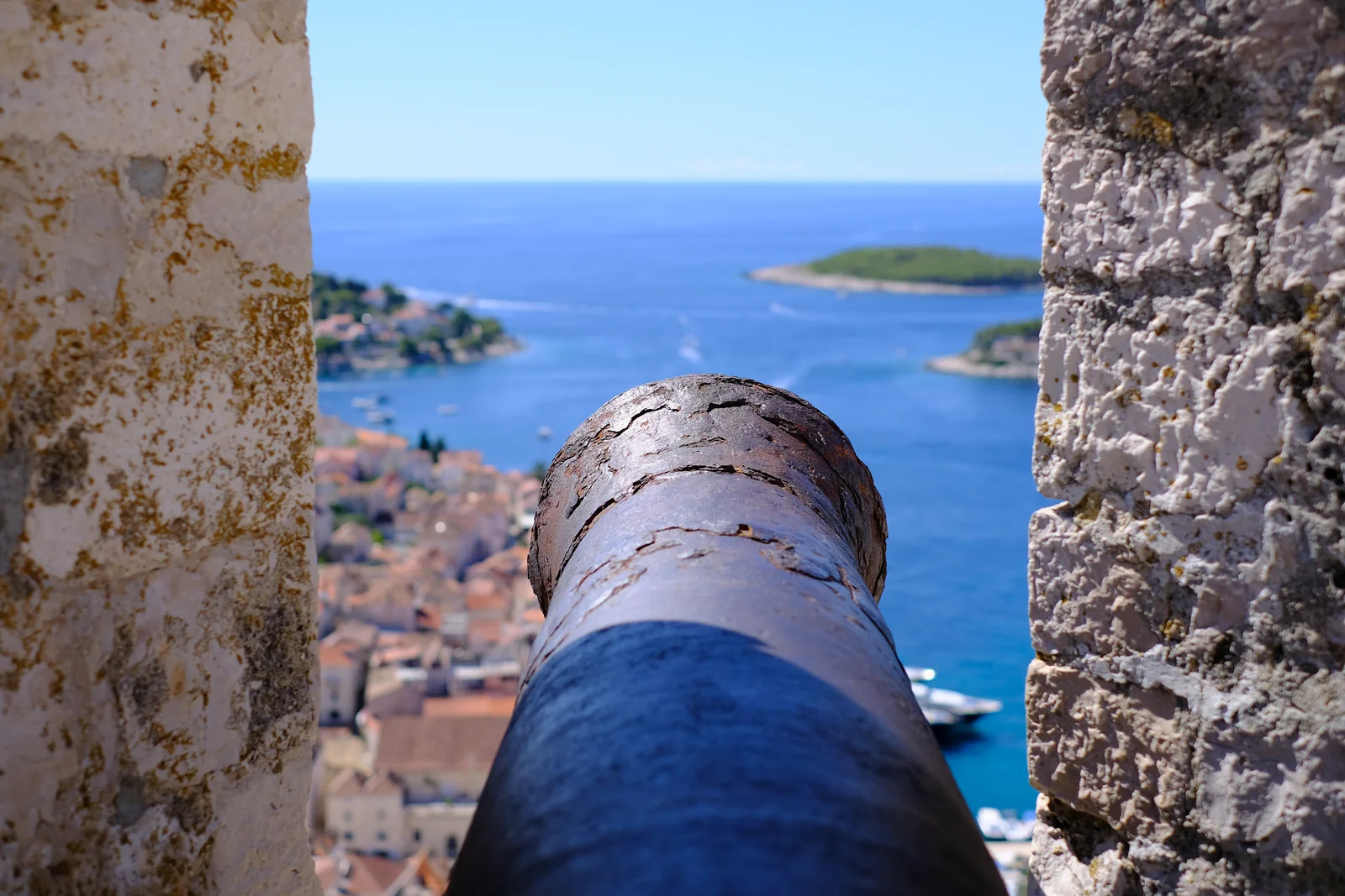 A cannon pointing through an opening in the fortress wall towards the harbour