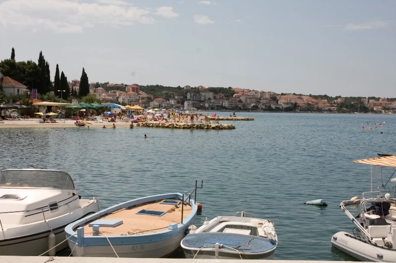 Okrug Gornji beach on Čiovo — sun umbrellas and swimmers, with the town behind