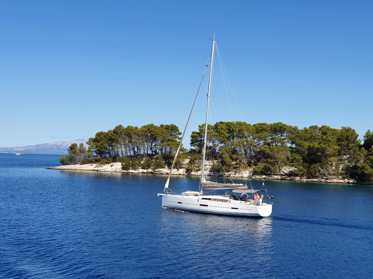 A sailing yacht anchored off a small pine-covered islet in deep blue water — a boat day out in Dalmatia