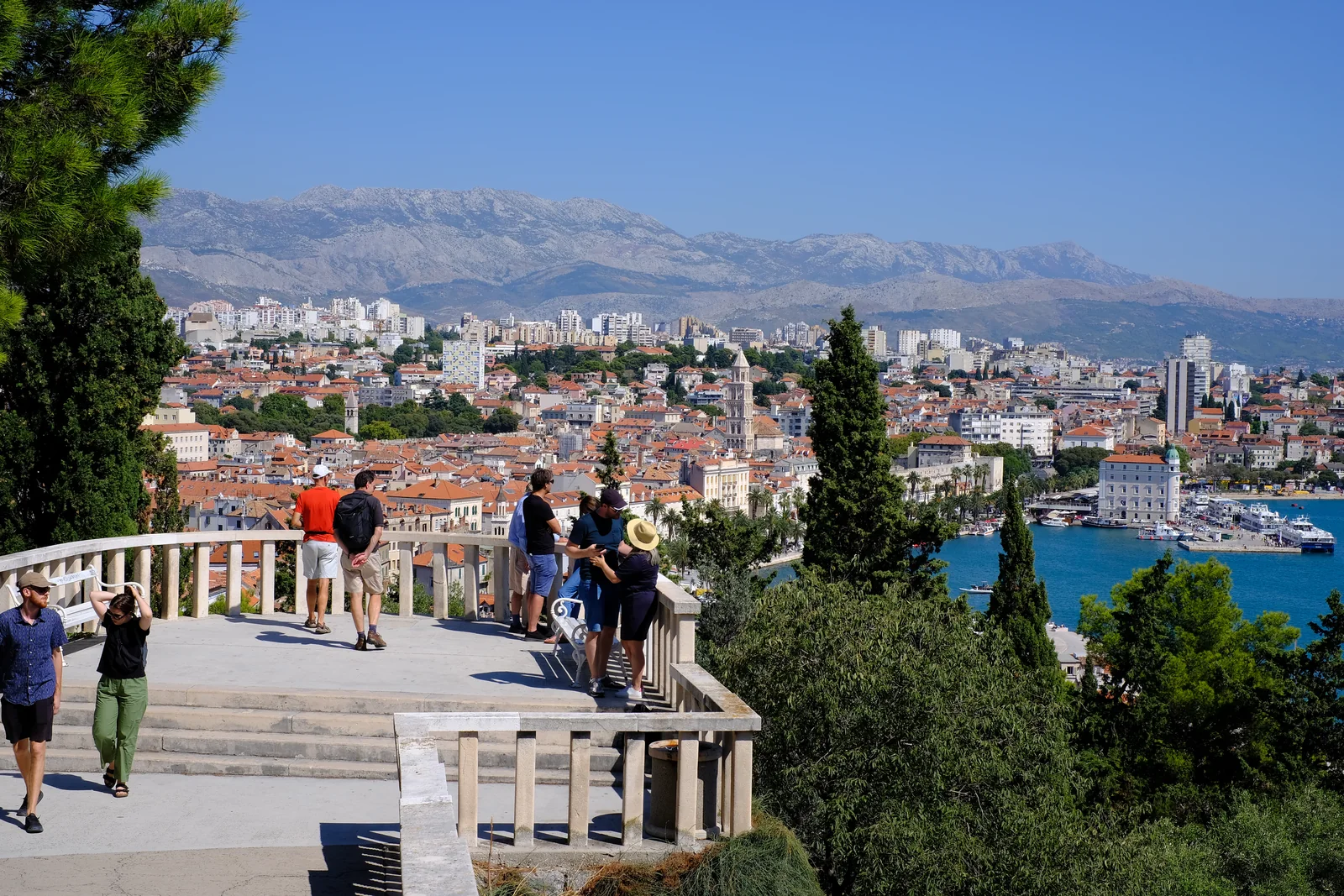 The stone terrace of the Marjan viewpoint with people looking out over Split's rooftops and the mountains behind