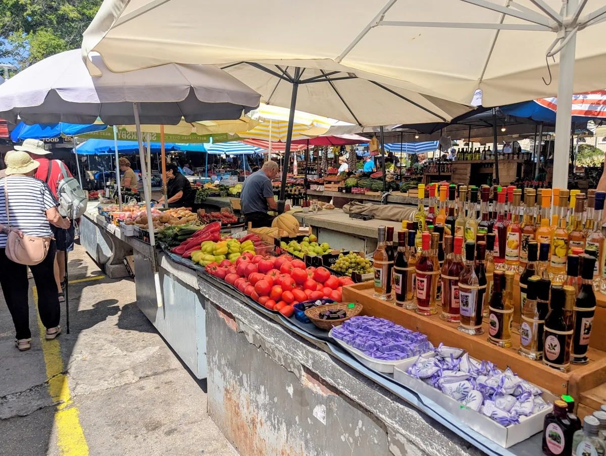 Stalls of tomatoes, fruit and bottled oils and liqueurs under white parasols at Trogir's green market