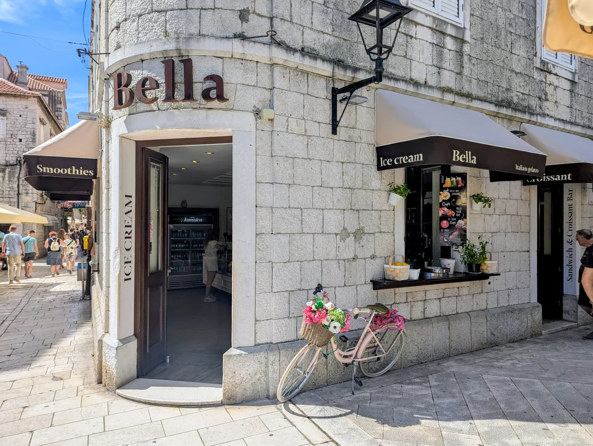 An ice cream shop on a corner of Trogir's old town, with awnings and a pink bicycle parked outside