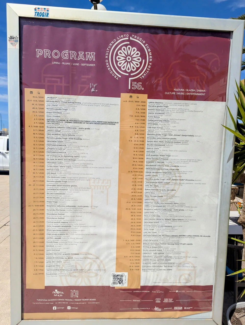 A printed summer programme poster in a glass case on a street in Trogir's old town